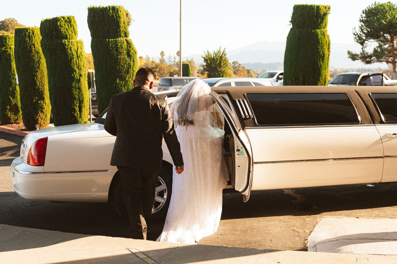 A couple walking towards their white stretch limousine after their wedding ceremony.