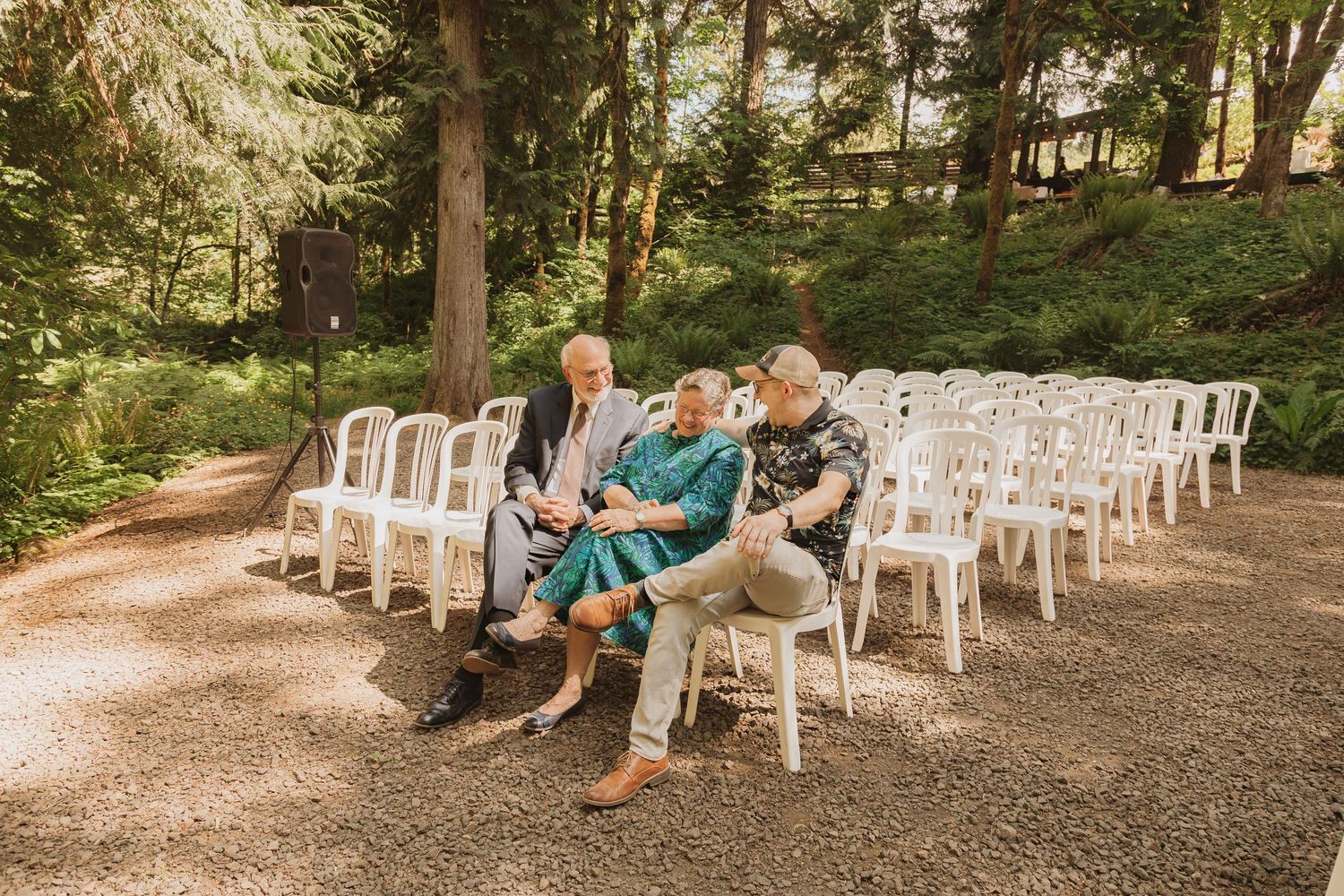 Guests seated in white chairs at an outdoor woodland wedding venue.