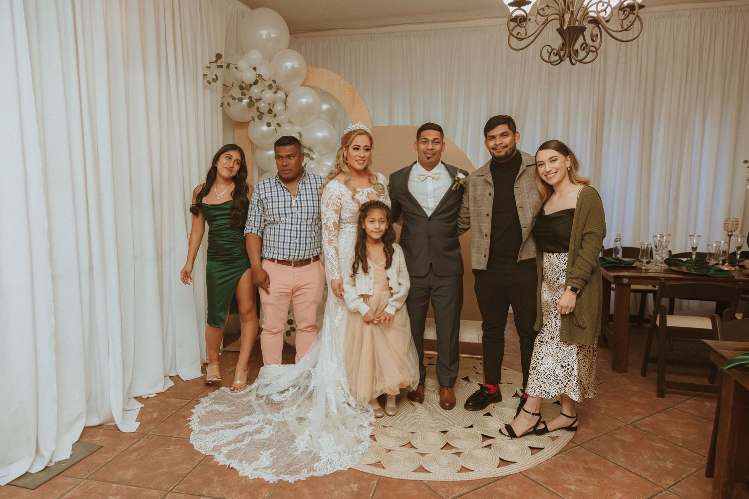 Wedding party poses together under decorative balloon arch in indoor venue.