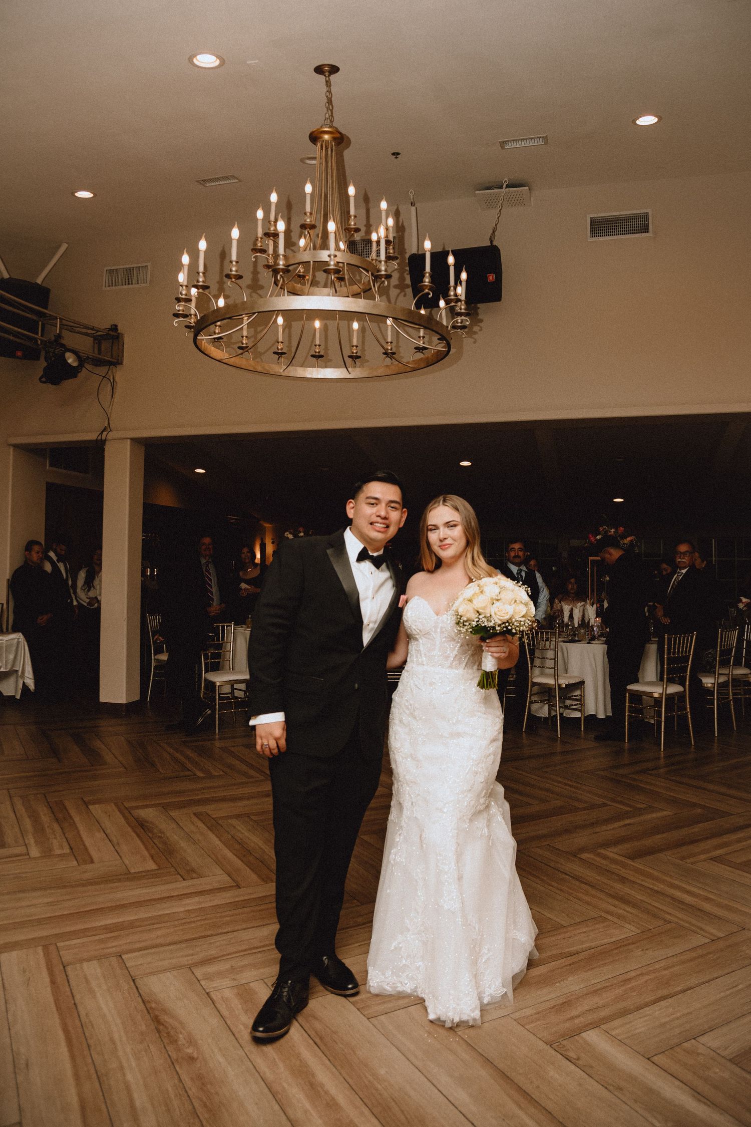 A wedding reception scene with an elegant chandelier and herringbone wood flooring.