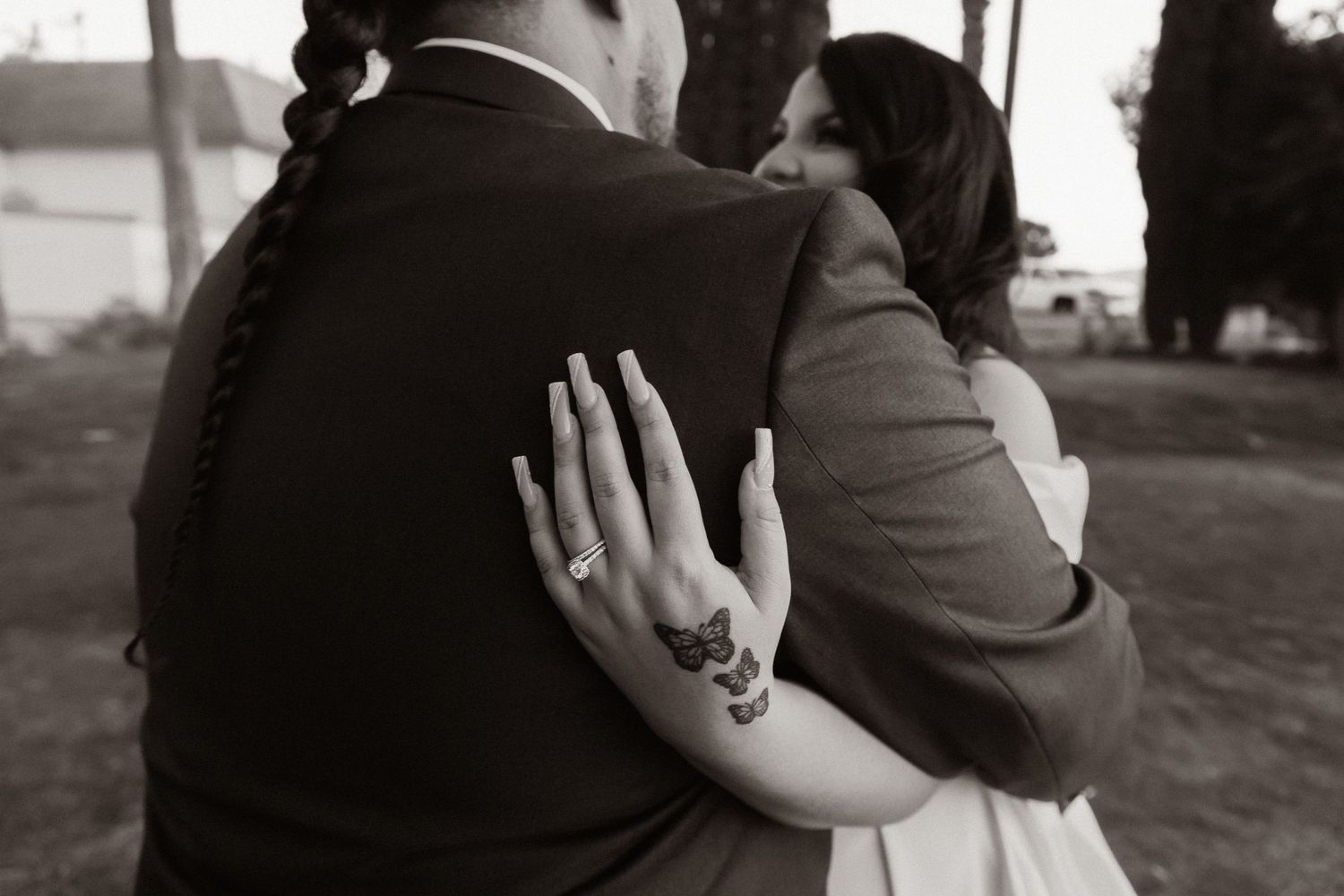 A black and white wedding photo capturing a tender embrace with a sparkling engagement ring visible.
