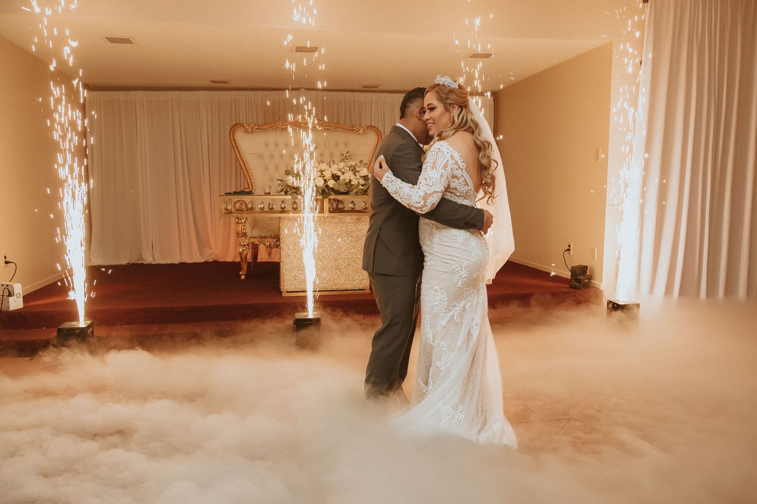 Couple embraces during their wedding dance surrounded by elegant decor and atmospheric fog effects.