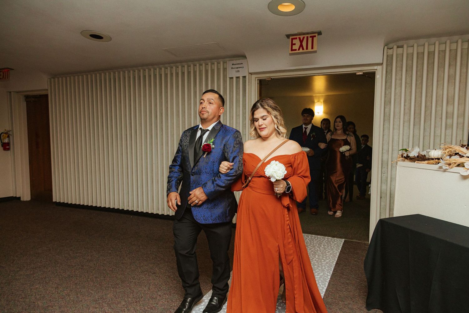 Wedding attendants make their entrance through doorway in bright formal attire.