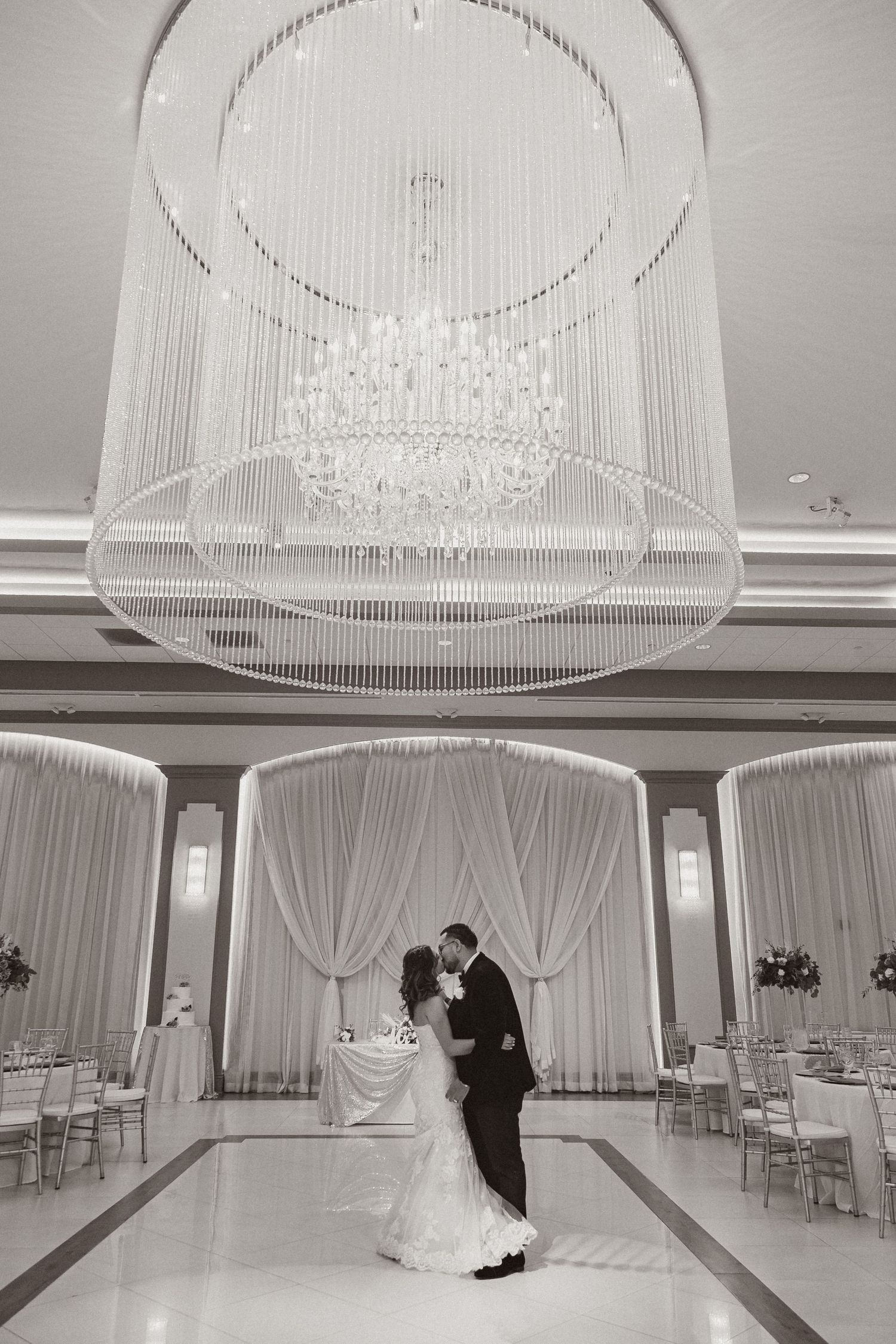 A tender wedding dance moment captured in black and white under an ornate crystal chandelier.