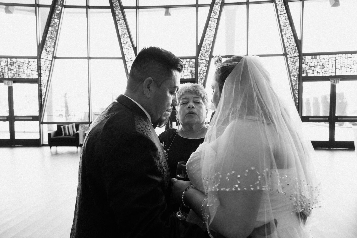 Black and white intimate moment during wedding ceremony with bright windows in background.