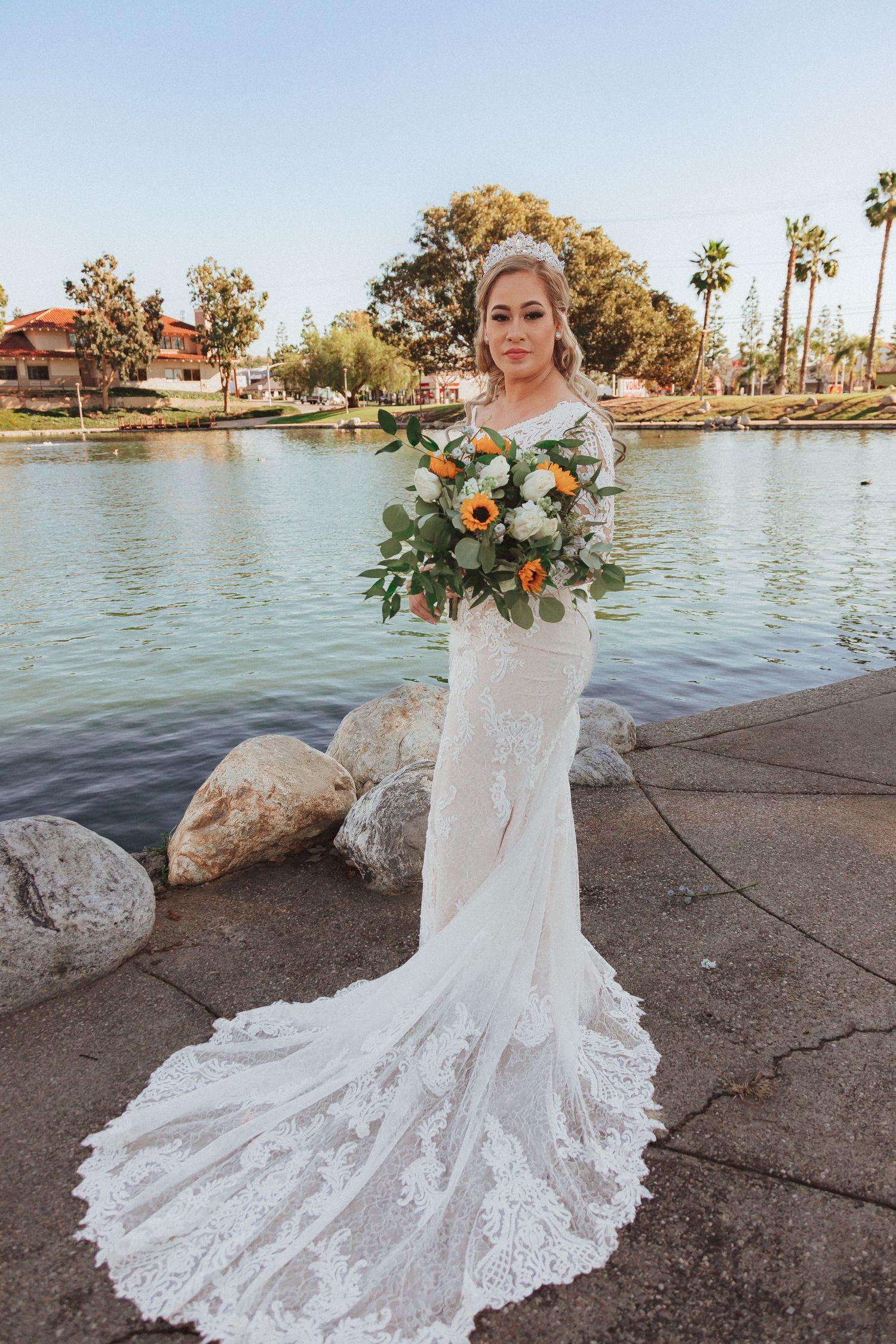 Elegant bridal portrait with lace wedding gown and colorful bouquet by scenic lake.