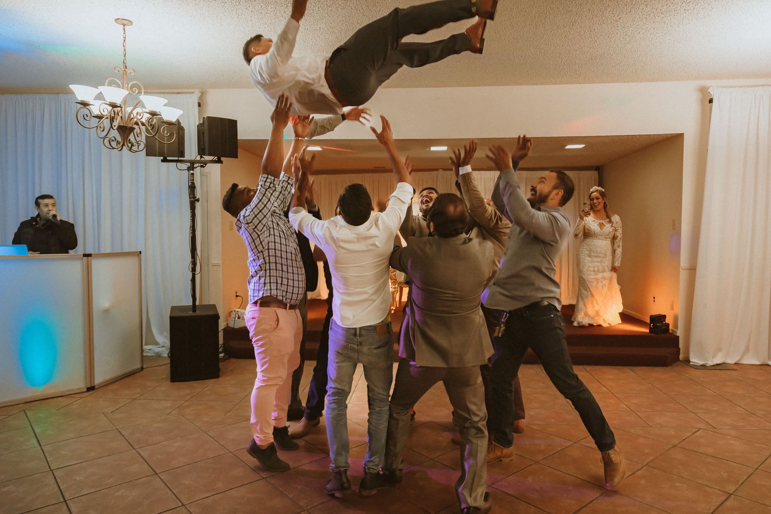 A group lifts and tosses someone into the air during a lively wedding reception celebration.