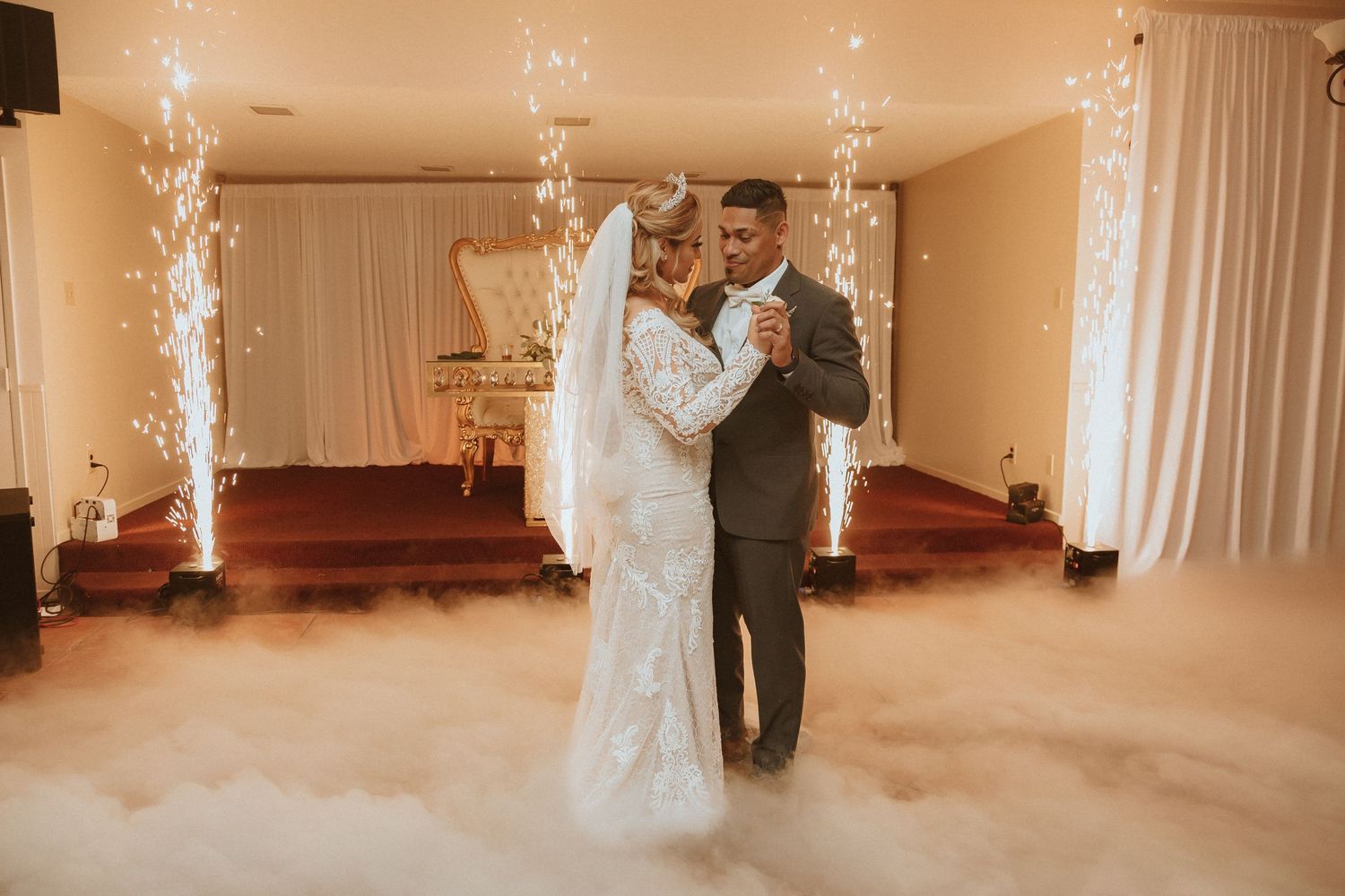 A romantic first dance in a dreamy wedding venue with sparkler fountains and fog effects creating a magical atmosphere.