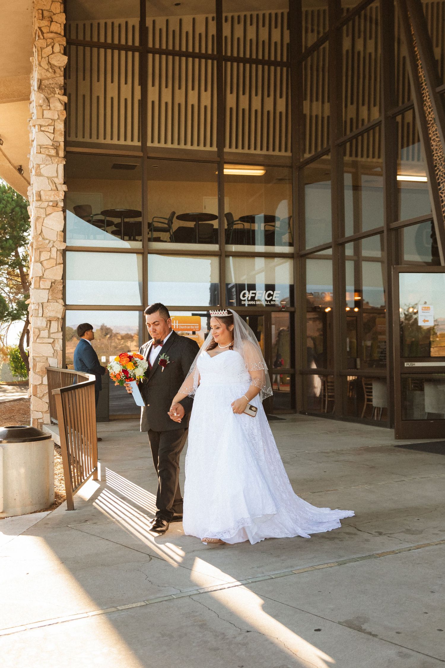 Sunlit exterior shot of wedding couple standing outside stone-accented church building.