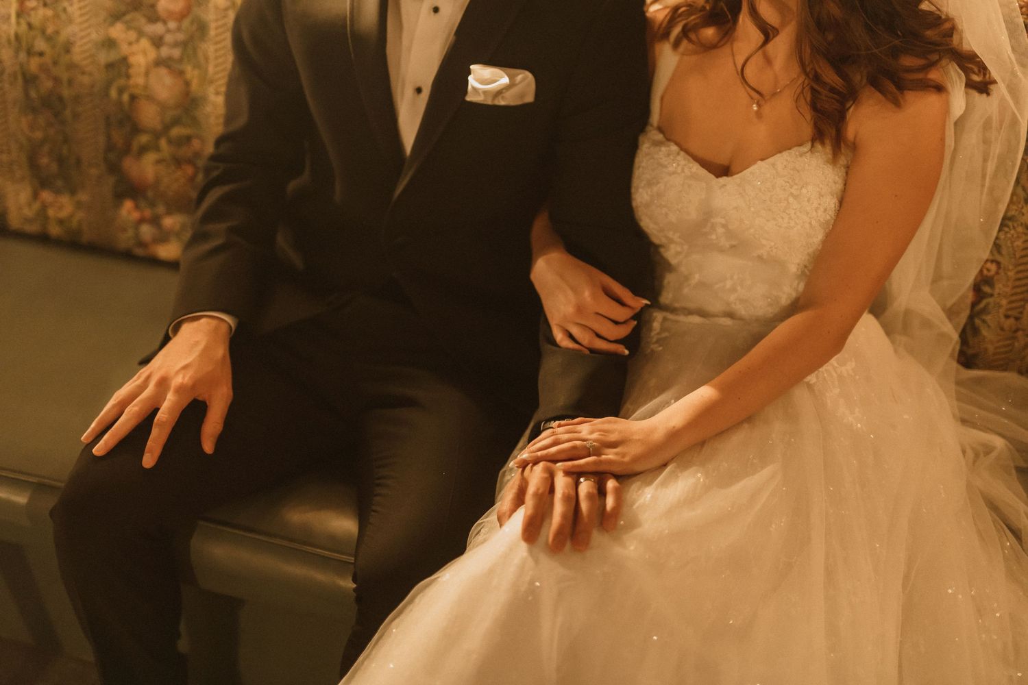 Detail shot of bride and groom sitting together with focus on wedding dress and hands.