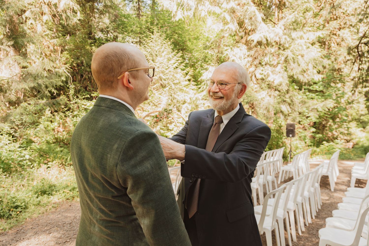 Two people sharing a warm moment before outdoor wedding ceremony with white chairs in background.