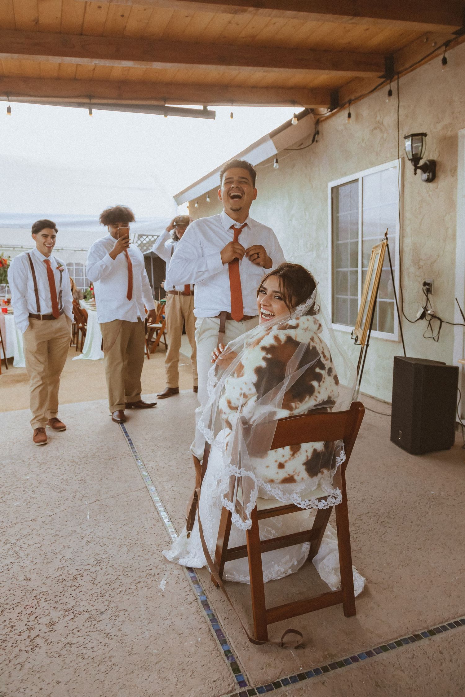 Guests in suspenders watch and laugh as a couple shares a joyful moment during their wedding reception.