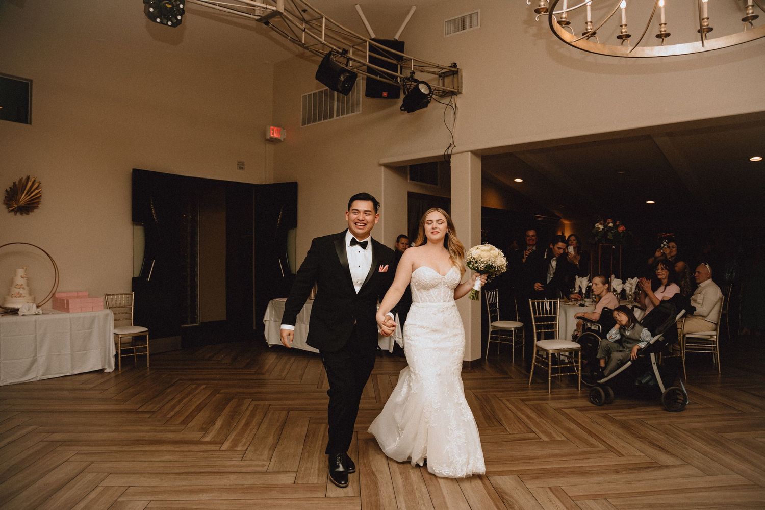 A couple makes their grand entrance into an elegant reception hall with herringbone wood floors.