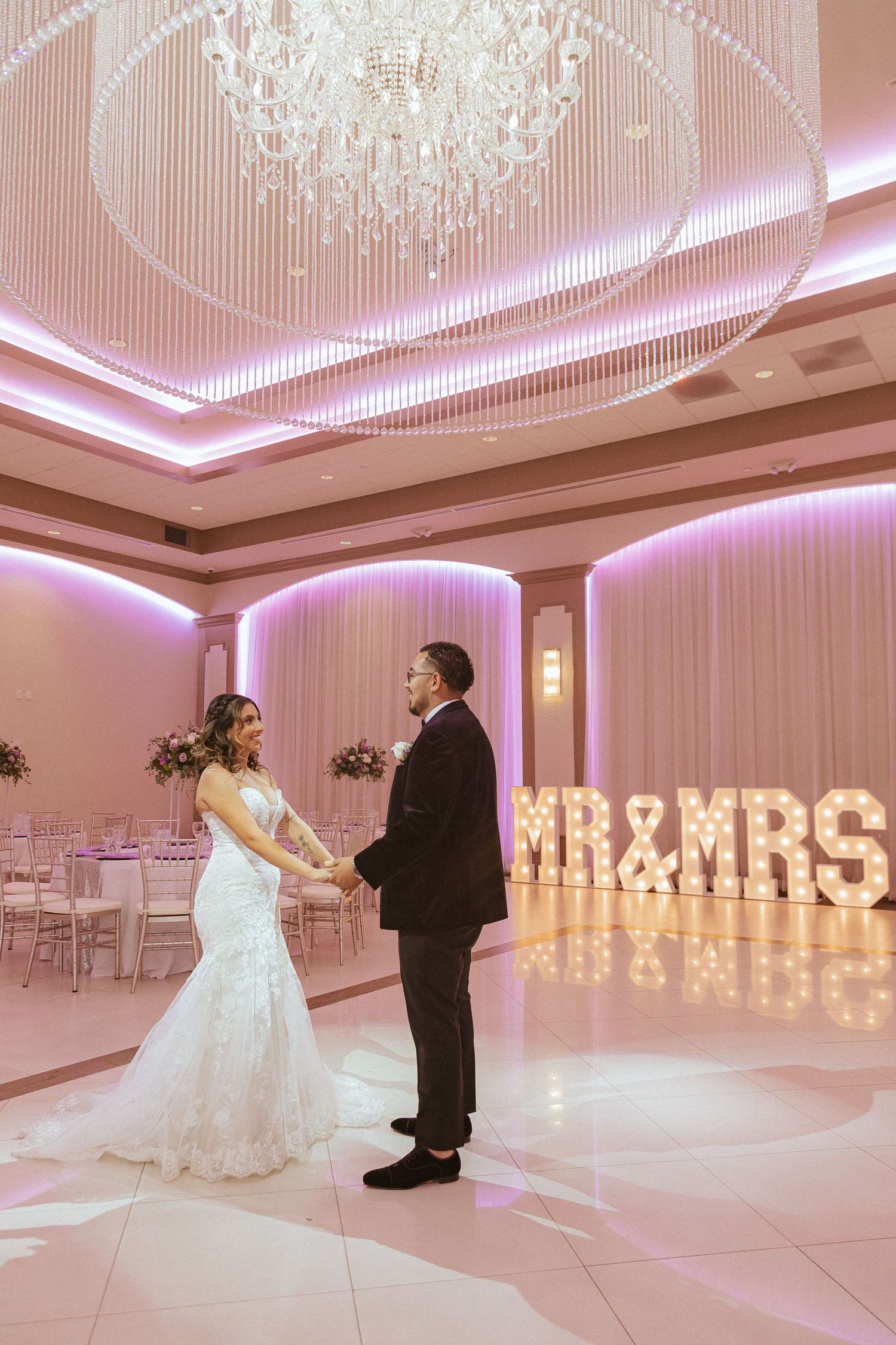 Luxurious ballroom with pink lighting and illuminated MR&MRS sign during a romantic wedding first dance.