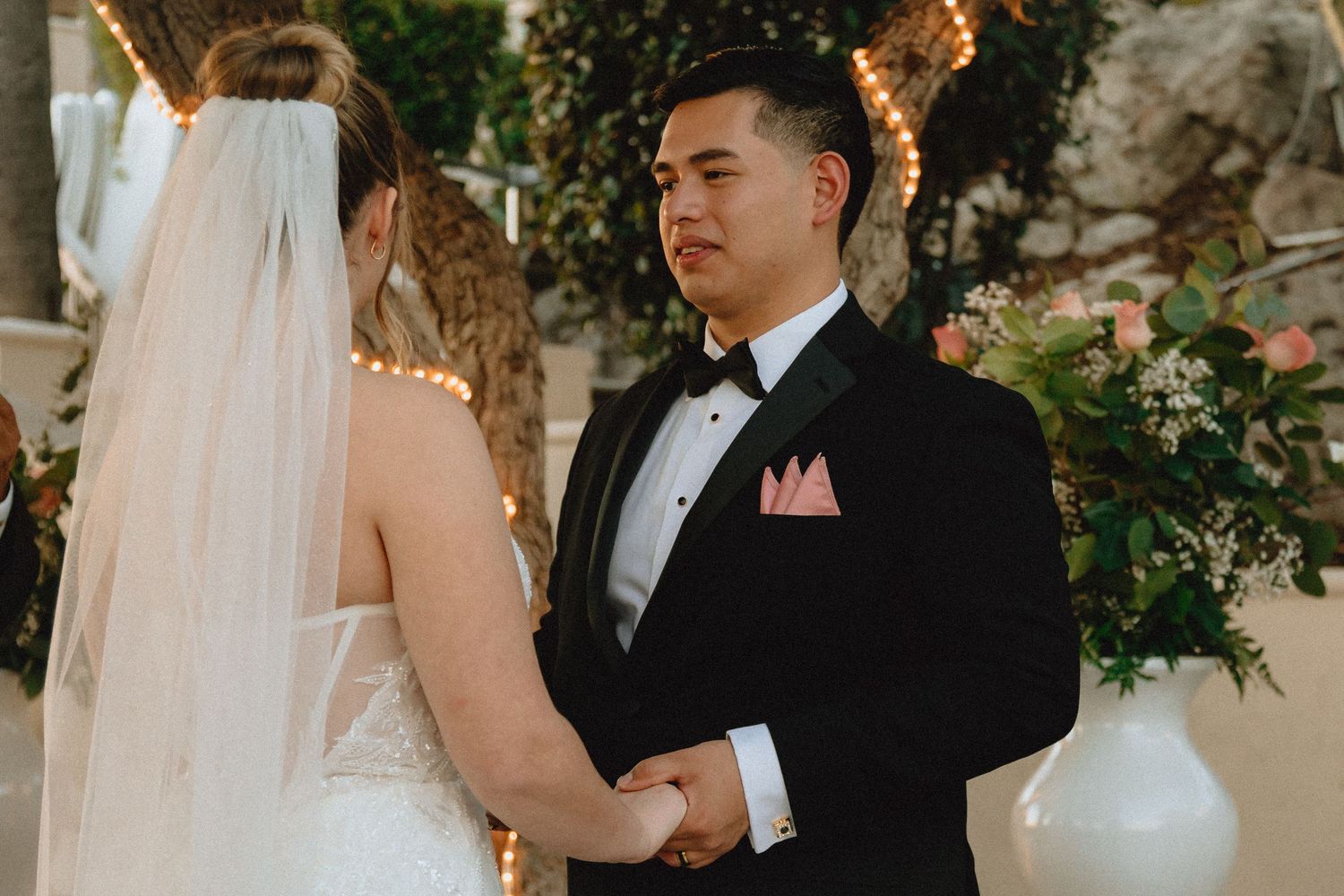 Intimate wedding ceremony moment under decorated trees with twinkling lights.