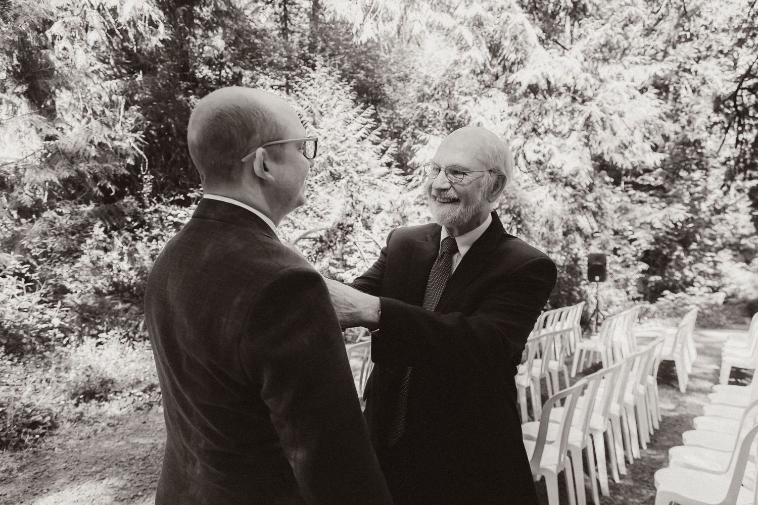 Black and white photo of two formally dressed people conversing at outdoor wedding ceremony.