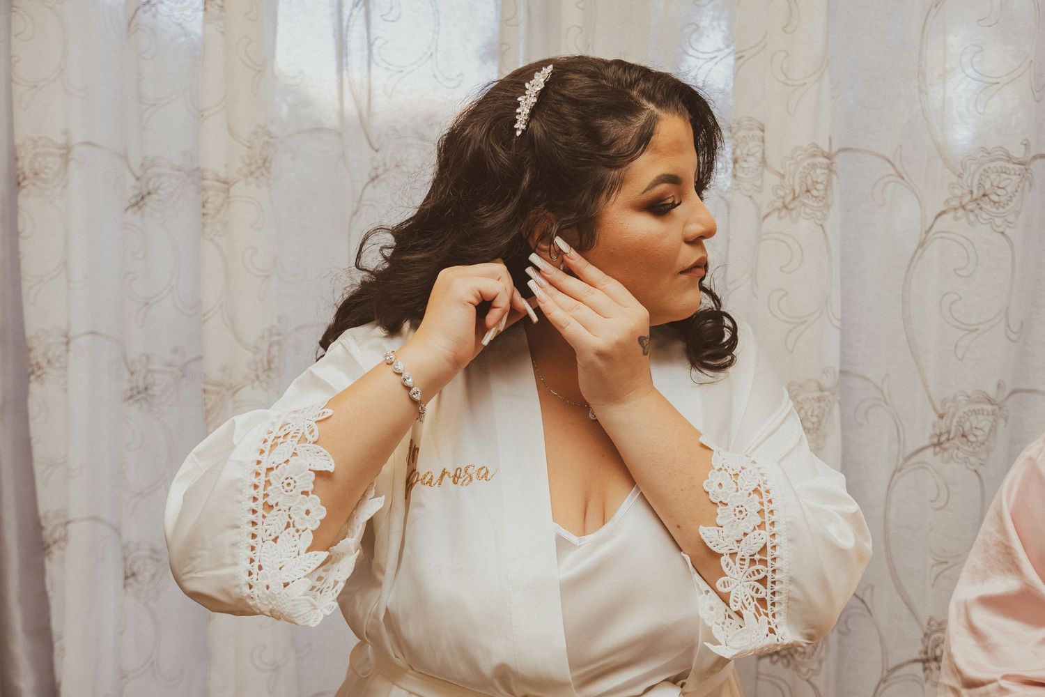 Close-up of bridal preparation showing lace sleeve details and jewelry adjustments.