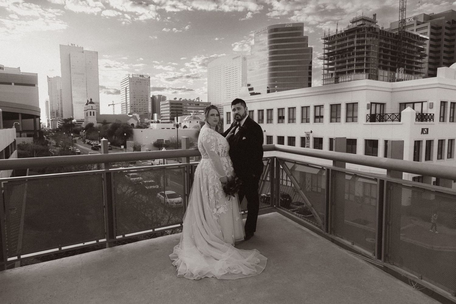 Black and white wedding photo captured on an urban rooftop with city buildings in the background.