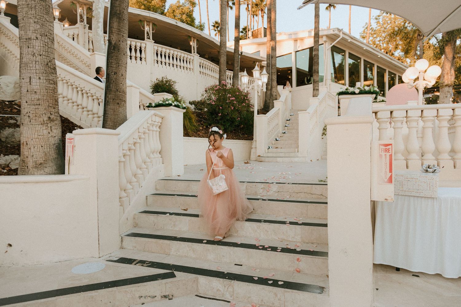 Person in flowing pink gown descends elegant white outdoor staircase.