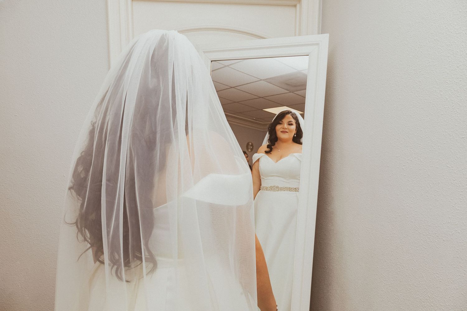 Ethereal shot of a bride looking in mirror with flowing veil in foreground.