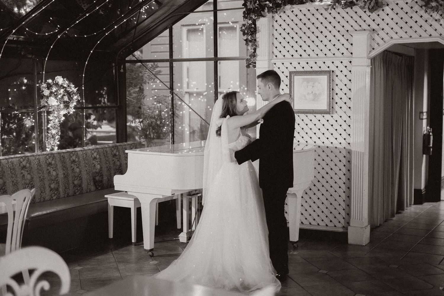 Black and white photo of wedding dance in elegant venue with piano and lattice backdrop.