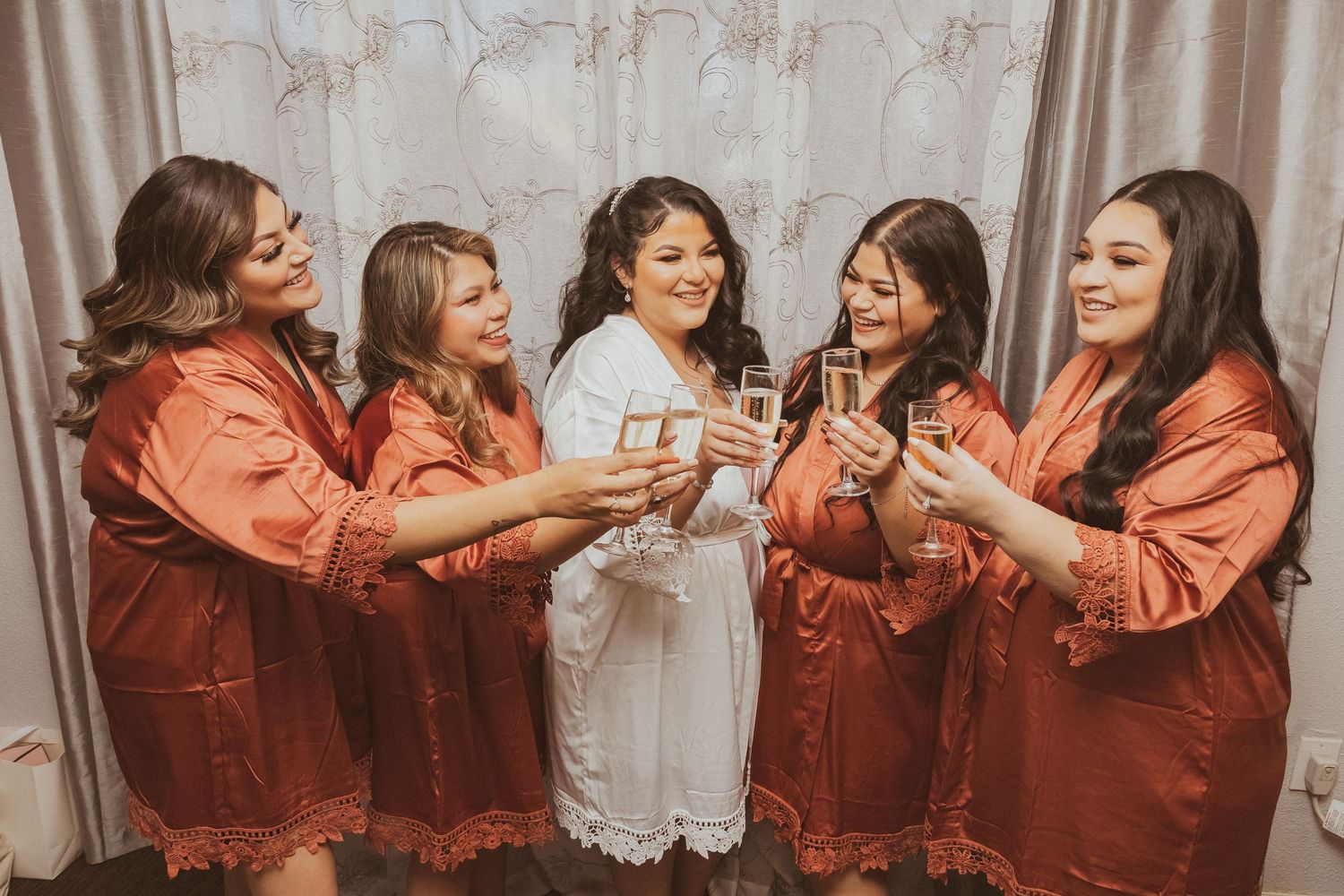 Candid moment of bridal party laughing while raising glasses in celebration.
