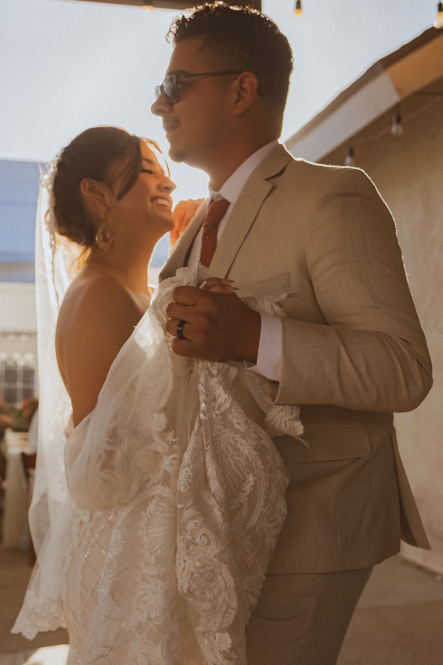 Romantic sunset portrait of couple in wedding attire embracing under arched walkway.