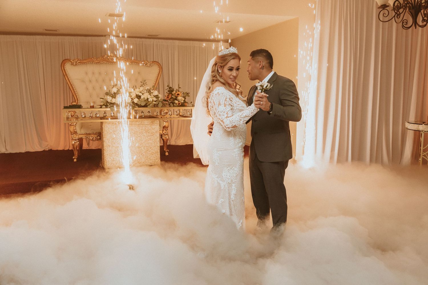 Couple embraces during wedding dance surrounded by ethereal fog and vertical sparkler fountains.