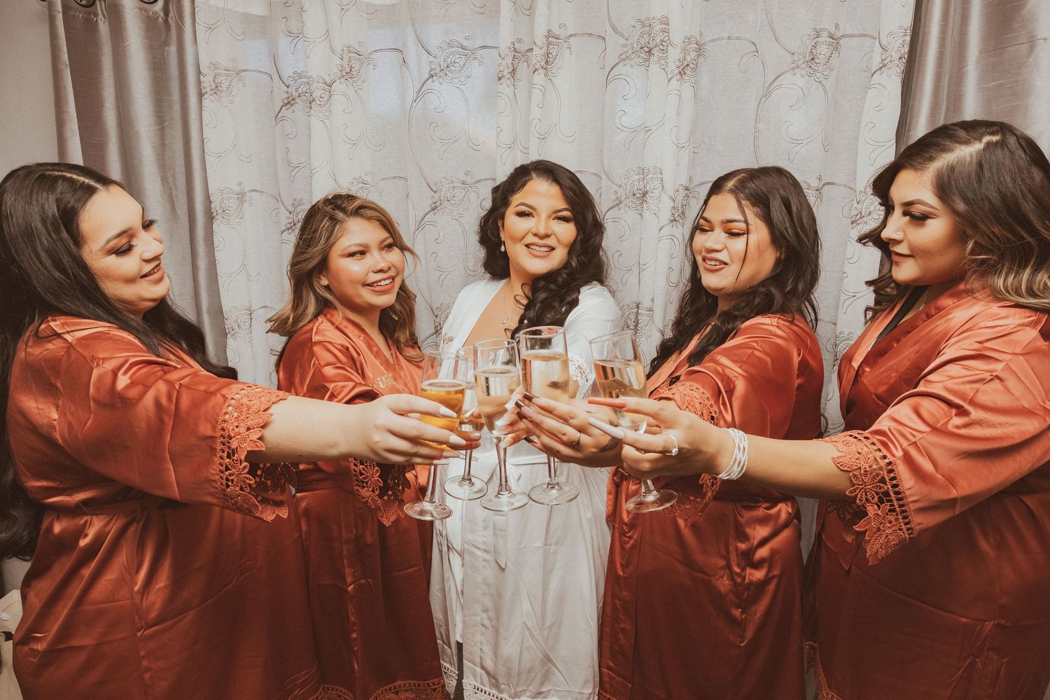 Wedding party wearing matching satin robes clinks glasses together in a circle.