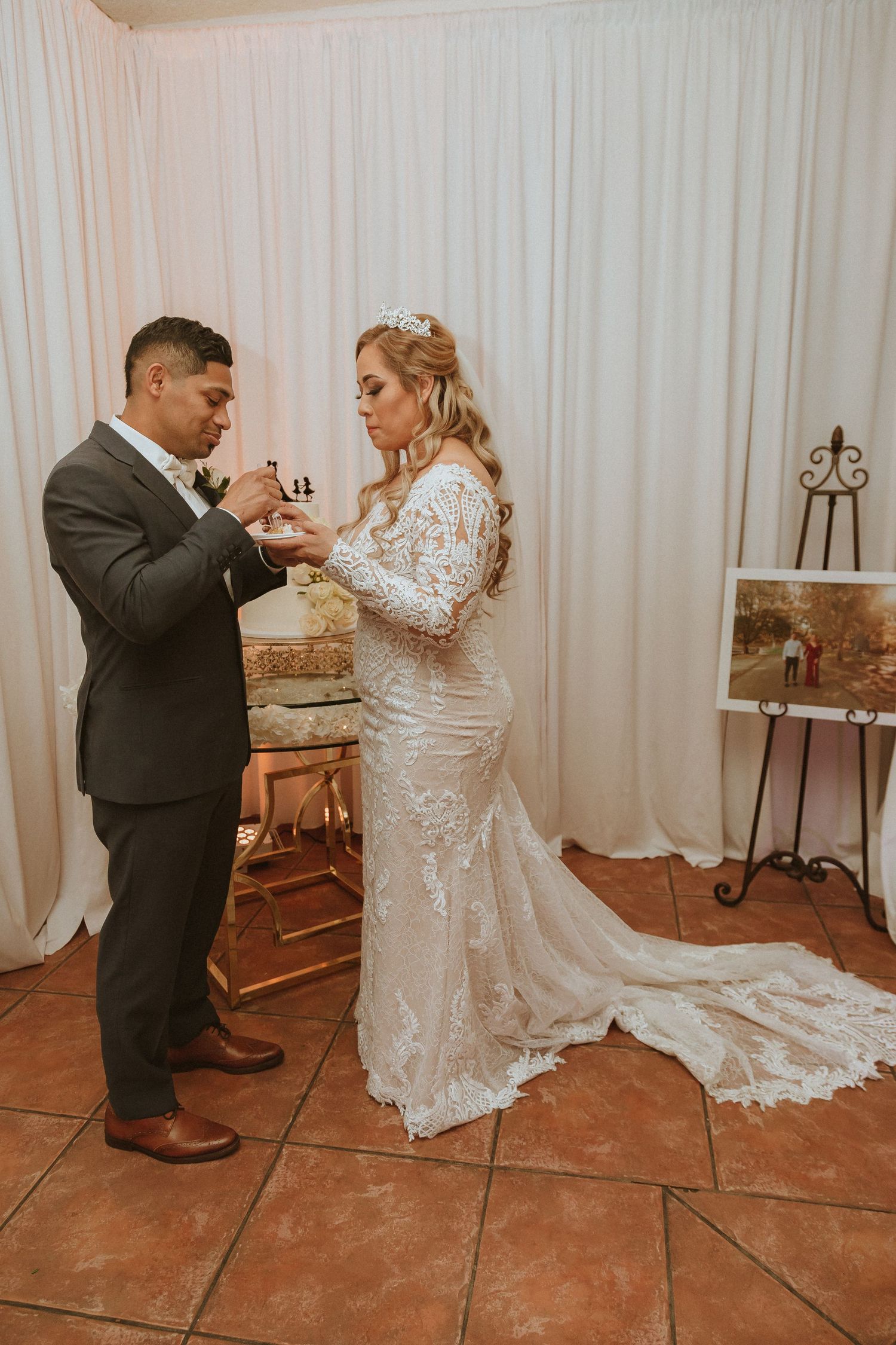 Couple sharing their first bite of wedding cake in front of a white backdrop.