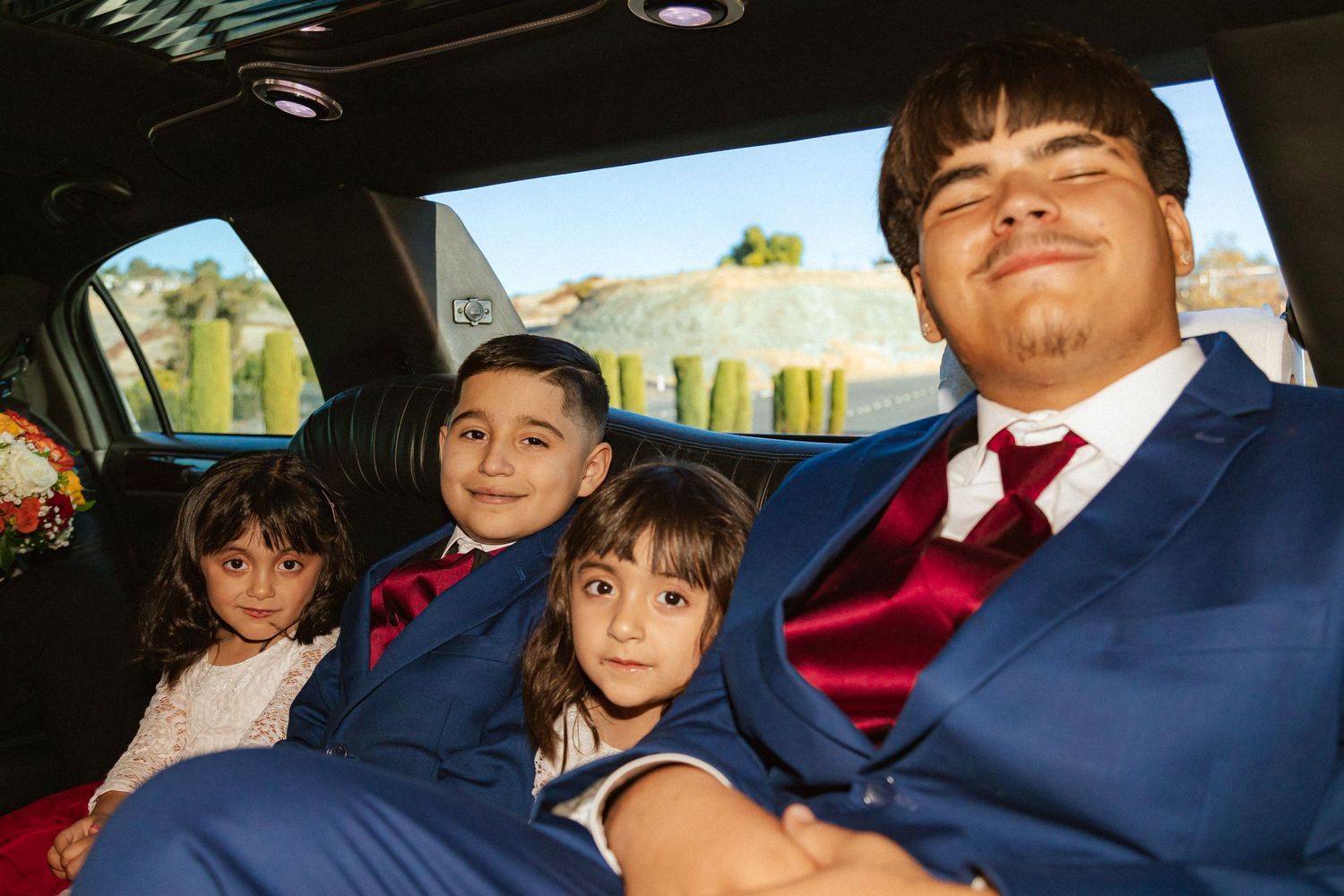 Young attendants in formal attire relax in a limousine during wedding celebrations.