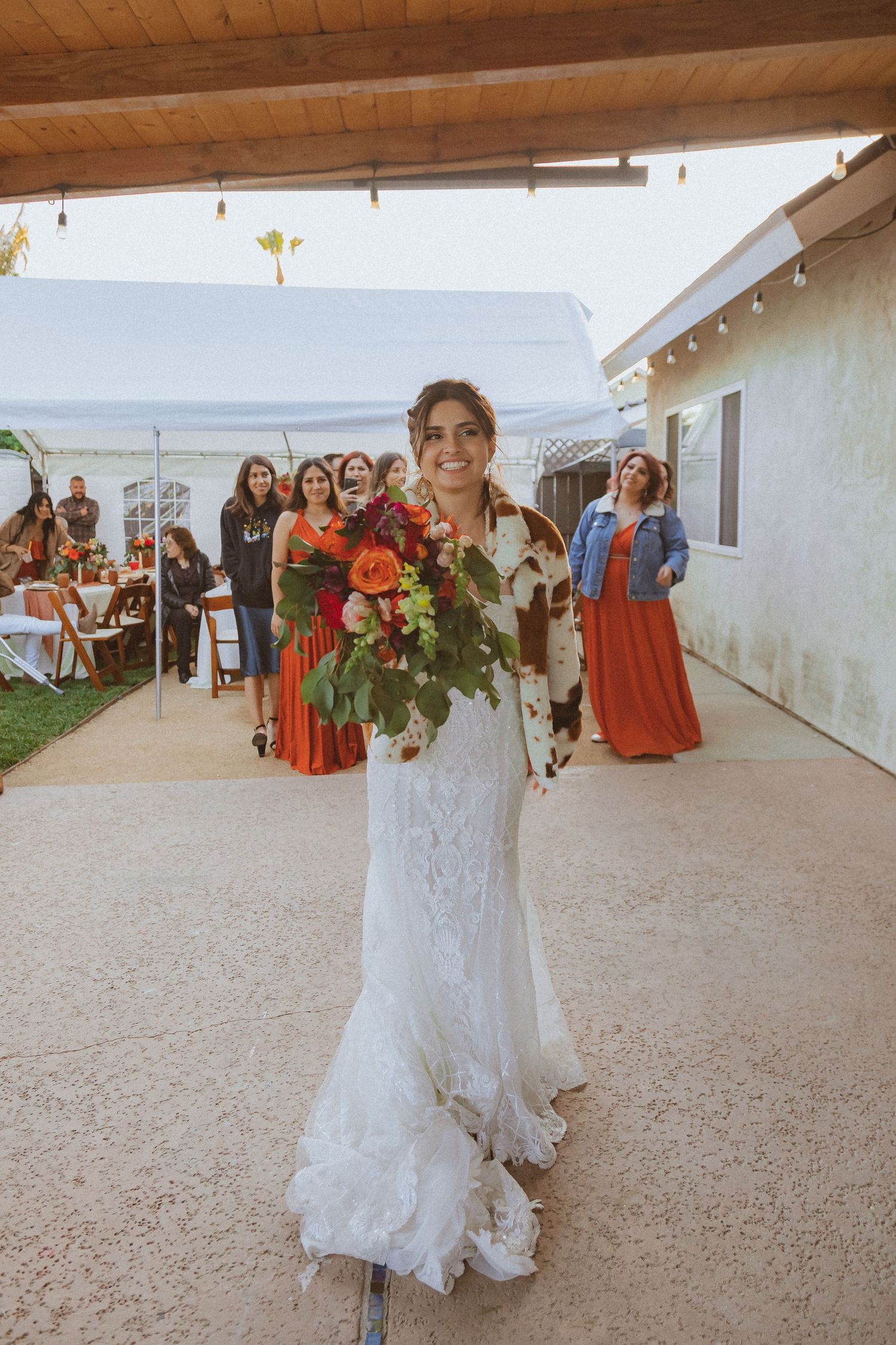 A bride in a lace wedding dress walking with a vibrant orange and red bouquet.