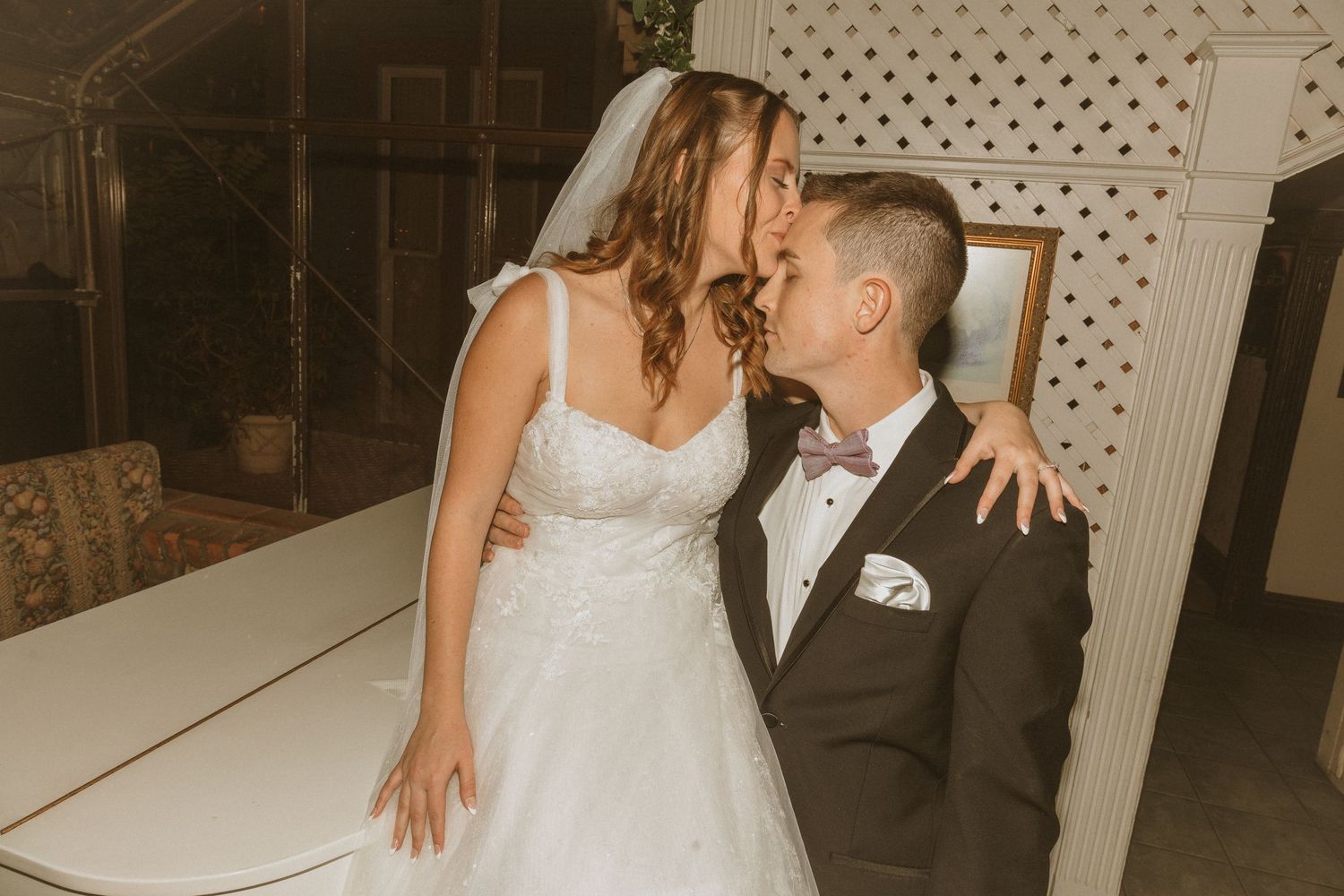 Romantic wedding moment captured between couple near decorative white lattice wall.