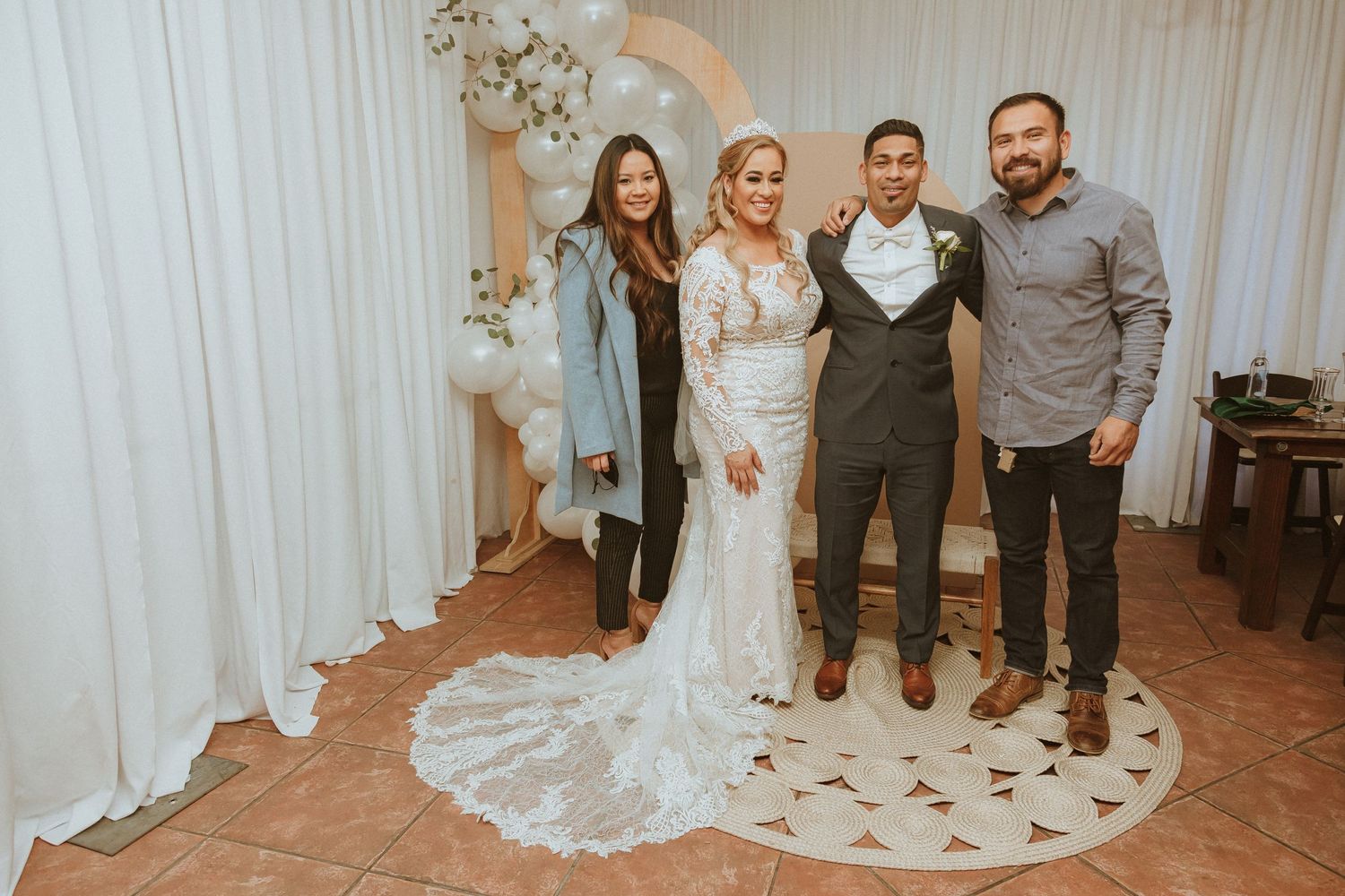 Small wedding group stands together in front of white backdrop with moon and balloon decorations.