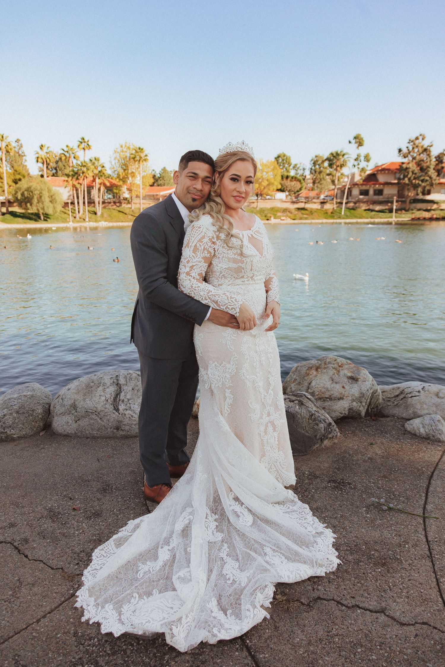 Romantic waterfront wedding portrait featuring couple in formal attire with lace gown.