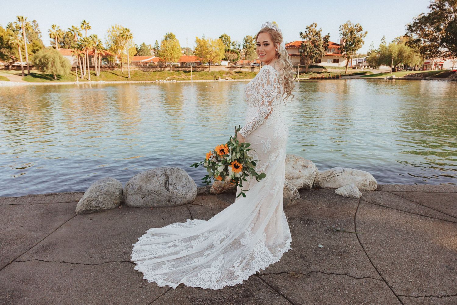 Stunning bridal portrait showcasing detailed lace gown with flowing train by waterfront.