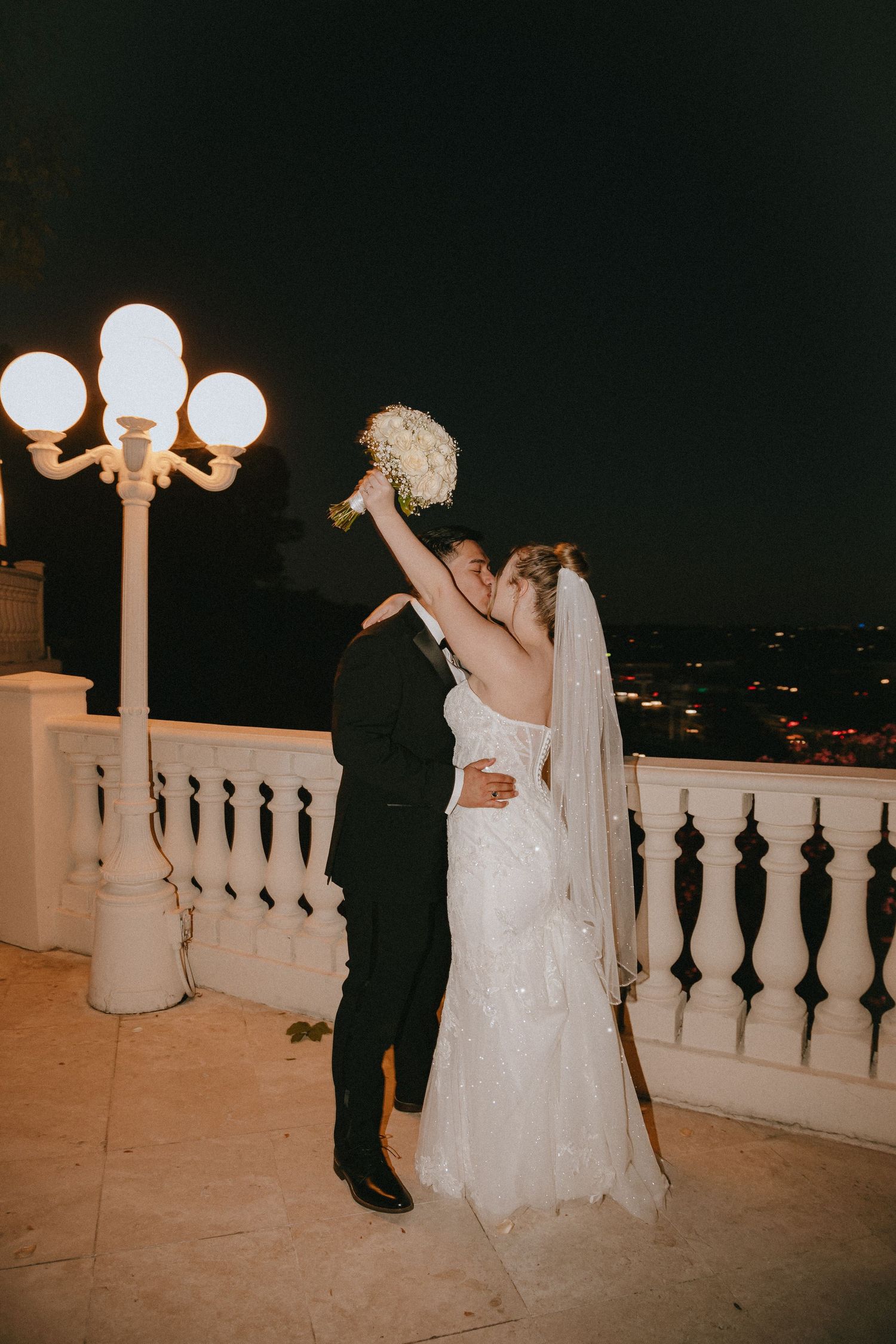 A joyful wedding celebration captured on an illuminated balcony with cityscape backdrop.