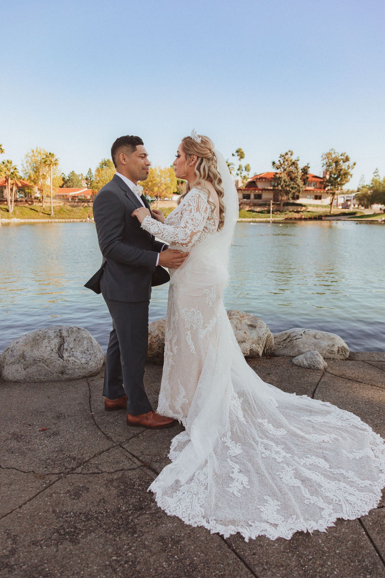 A romantic wedding moment captured by a lake with a stunning lace dress train.