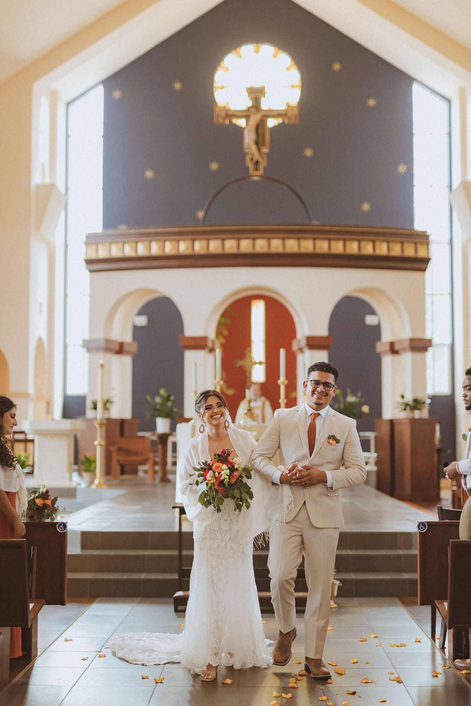 A couple walking down the church aisle after their wedding ceremony with rose petals scattered on the floor.