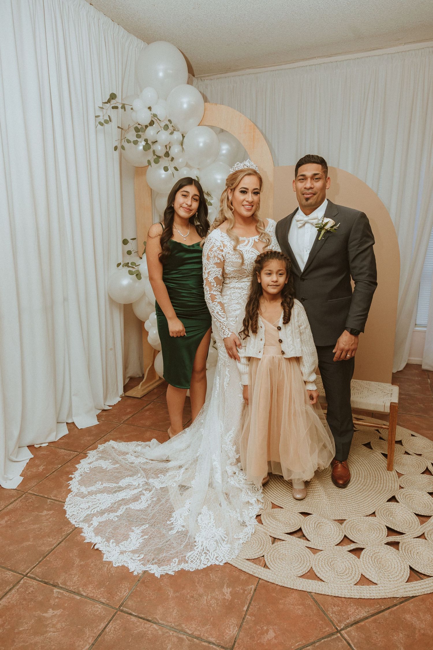 Wedding photo with bride in white lace gown standing with guests by decorative moon backdrop.