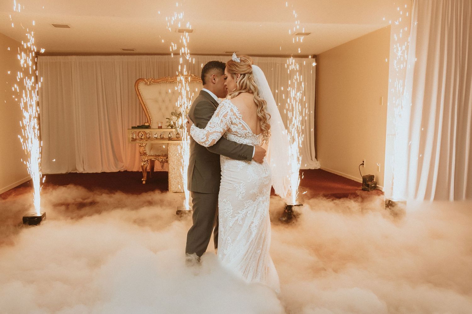 Couple shares first dance in beautiful reception venue with dramatic fog effect and sparkling fountains.