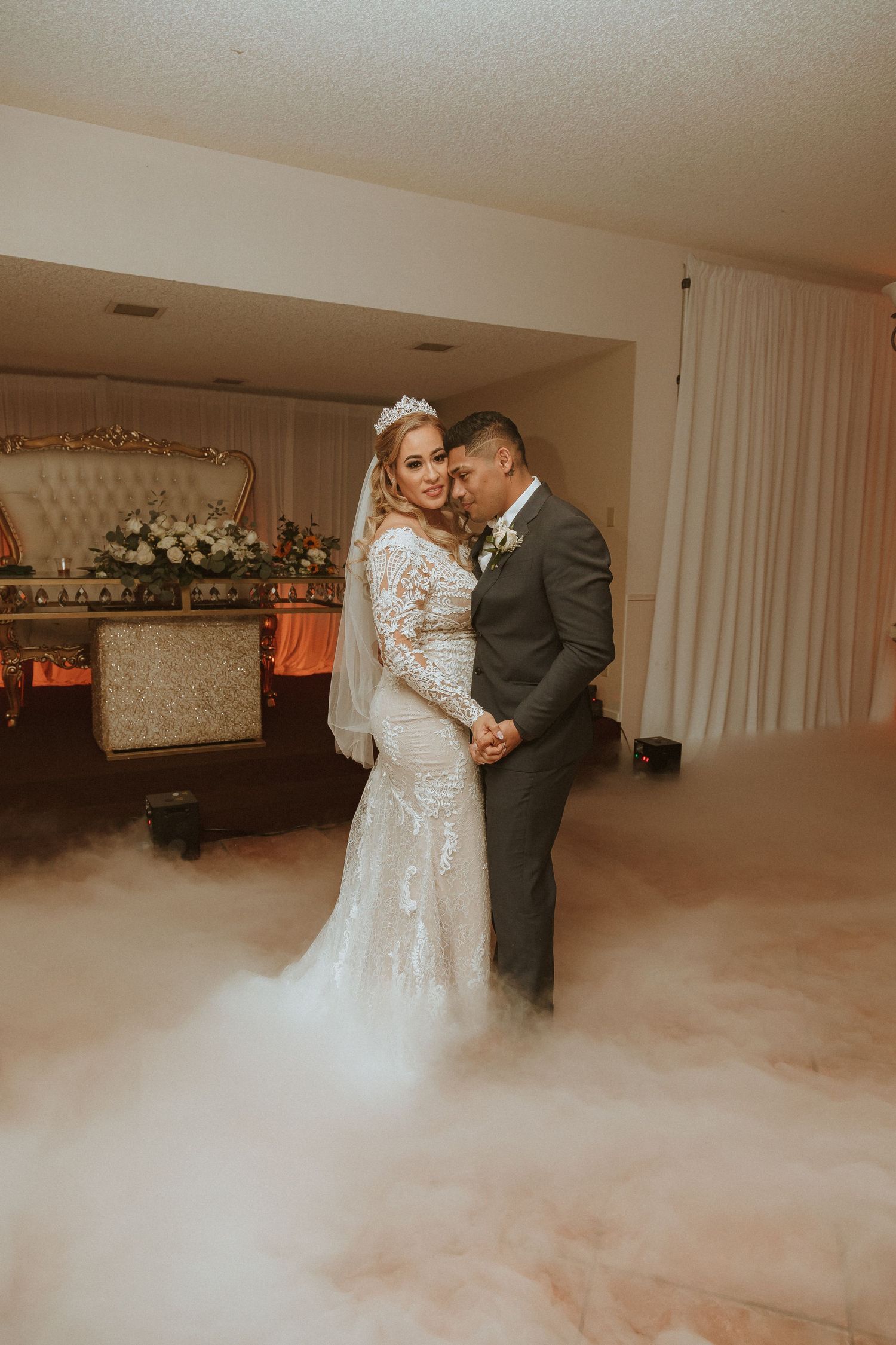 Intimate wedding moment captured in warm tones with fog effects and elegant vintage-inspired backdrop.