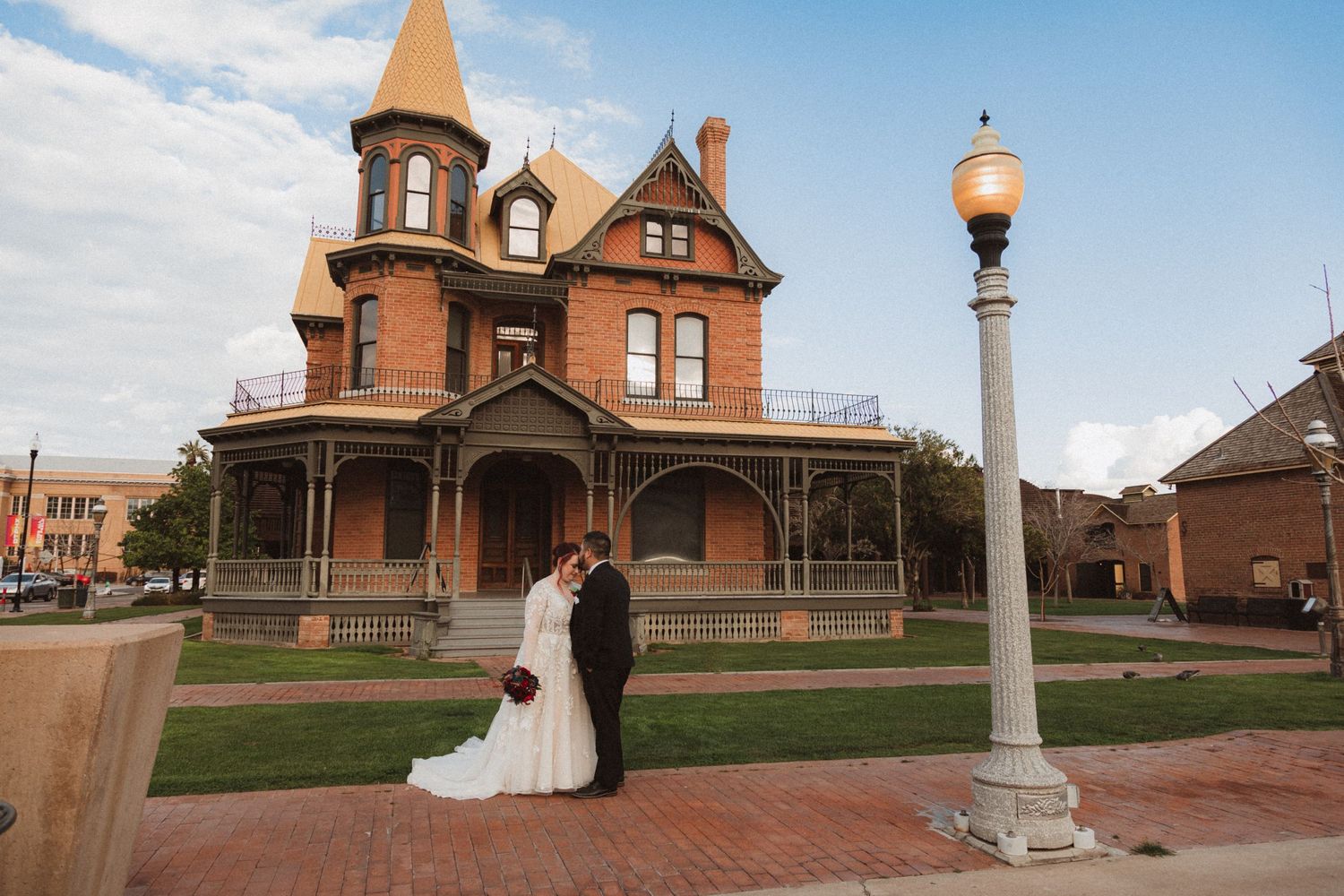 A sunset wedding photo at a historic Victorian mansion with street lamp in foreground.