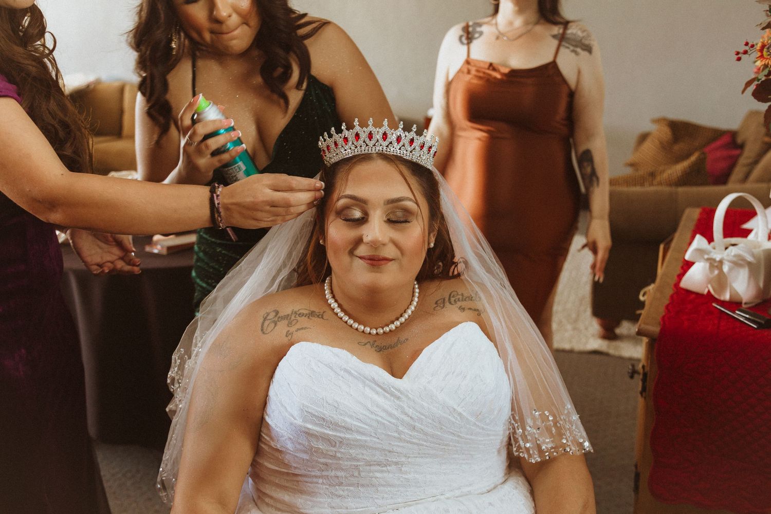 A bride wearing a tiara gets ready with help from her wedding party.