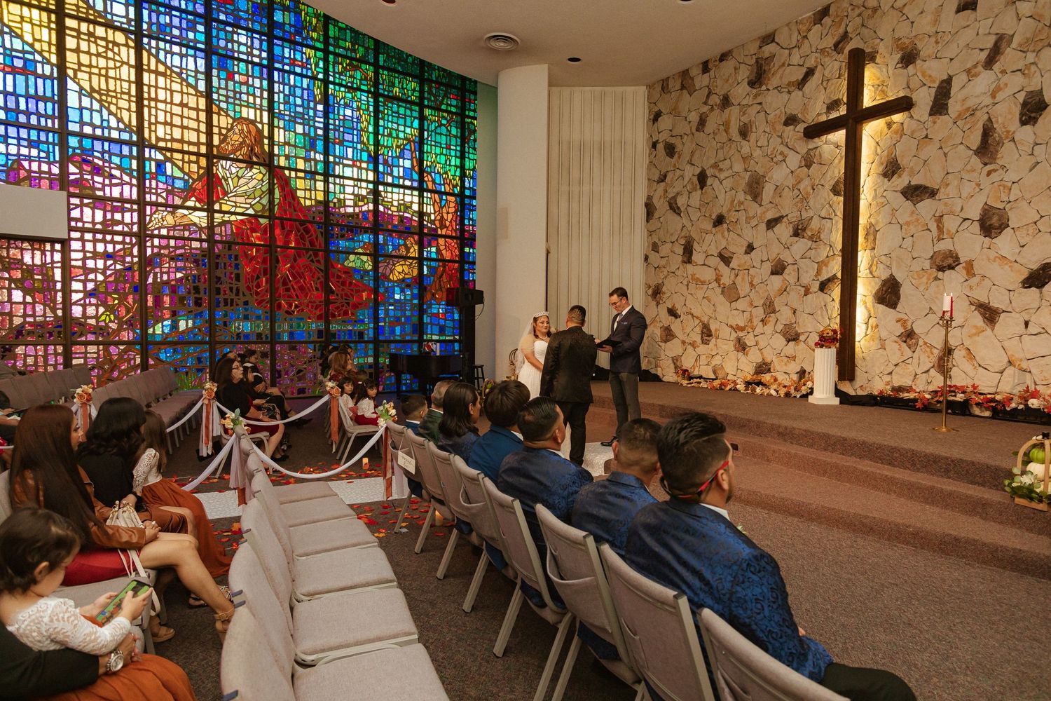A church interior with colorful stained glass windows and stone walls during a wedding ceremony.