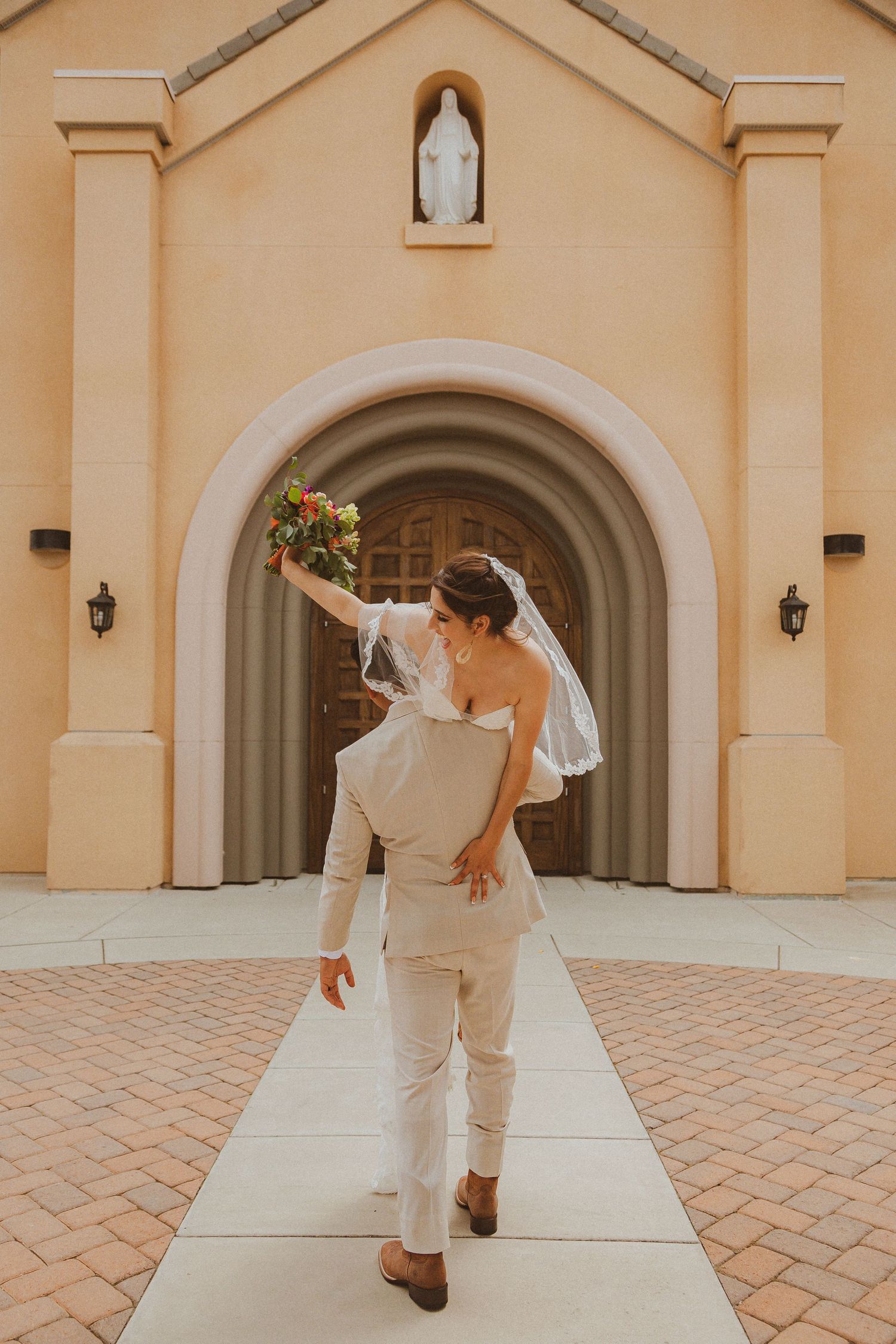 Celebratory lift pose by newlyweds in front of a church entrance.