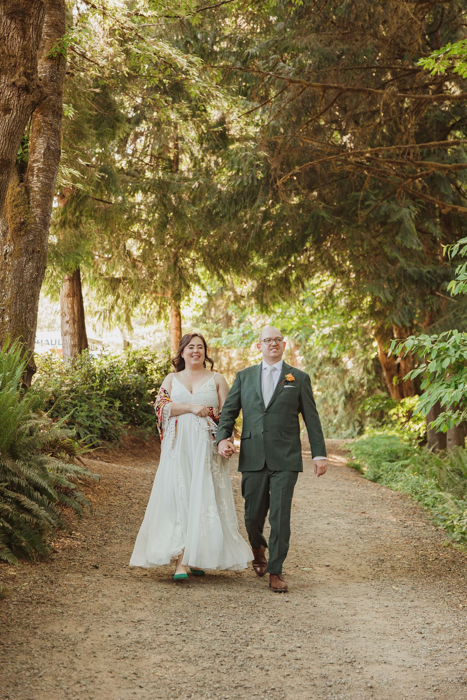 A couple walks hand in hand down a forest path during their wedding.