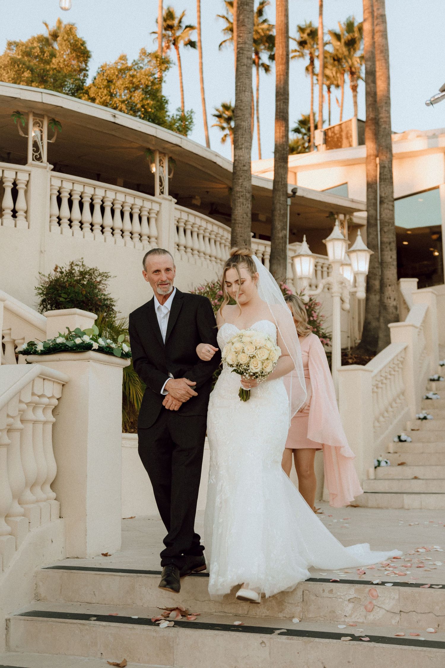 Elegant wedding moment captured on white stone steps with palm trees and lanterns.