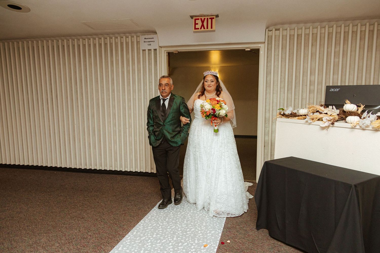 Traditional wedding processional down decorated hallway with reception table in background.