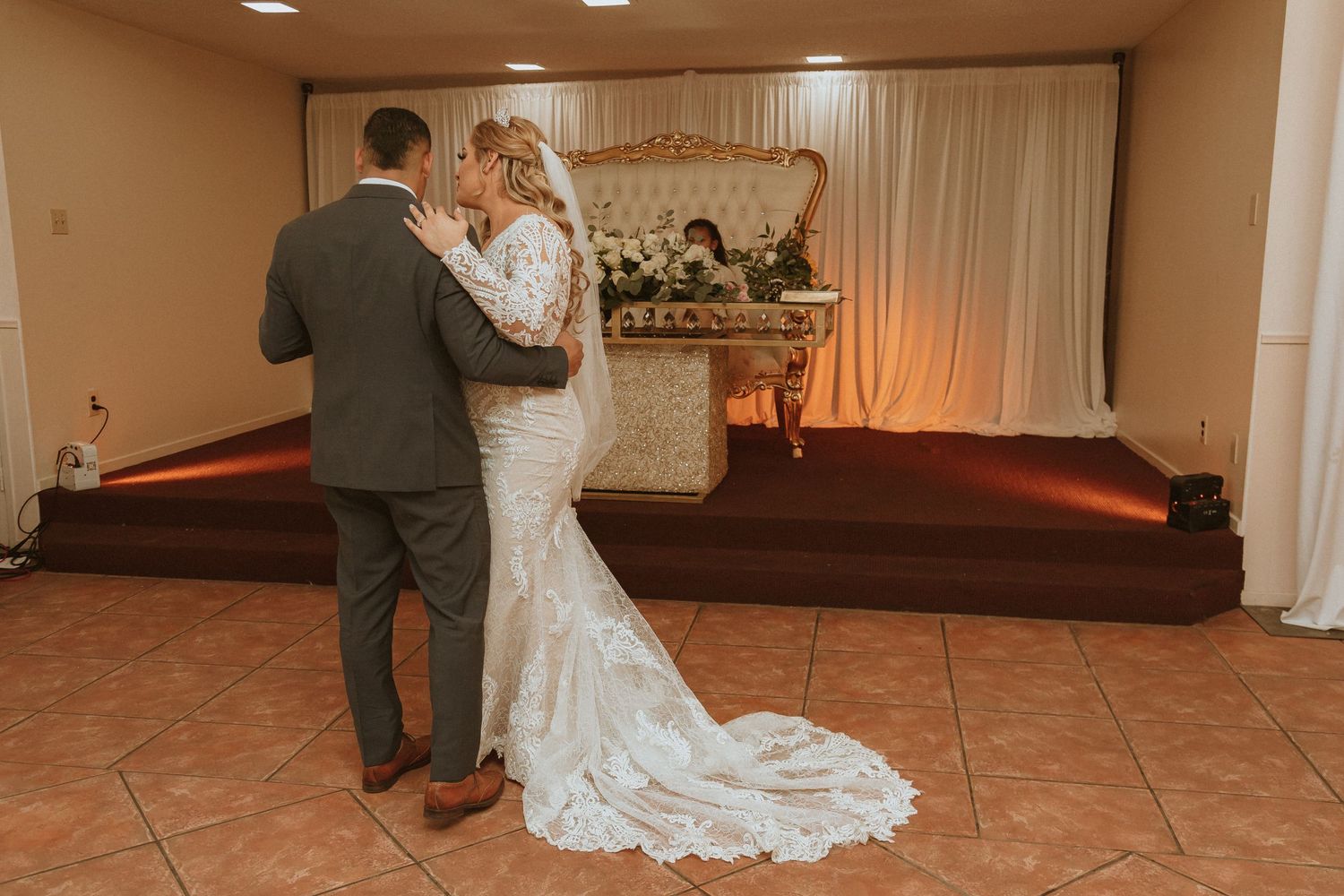 A romantic first dance at a wedding reception with the bride wearing an elegant lace gown with a long train.